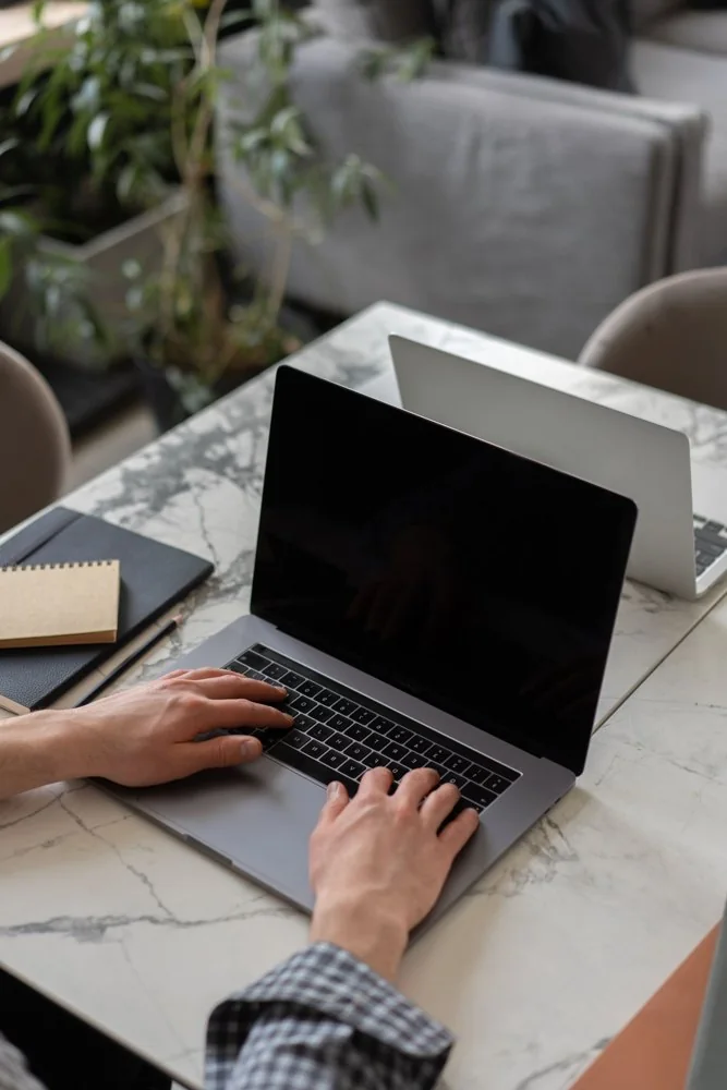 Hands using a laptop beside a notebook on a marble desk